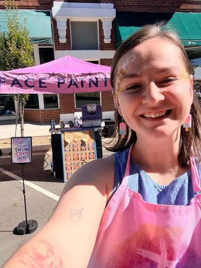 Ashley at her pink In His Image face painting booth at an outdoor event, face painting by In His Image, Morristown TN
