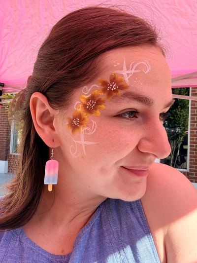 Golden flower and white swirl cross design on the temple, face painting by In His Image, Morristown TN