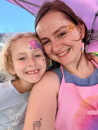 Ashley and a smiling girl both wearing flower and butterfly face paint, face painting by In His Image, Morristown TN