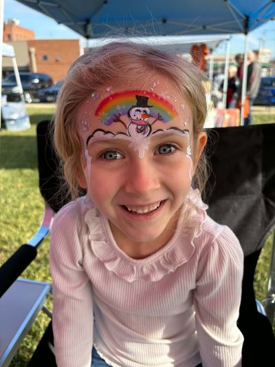 Girl with a rainbow and snowman forehead design at an outdoor event, face painting by In His Image, Morristown TN
